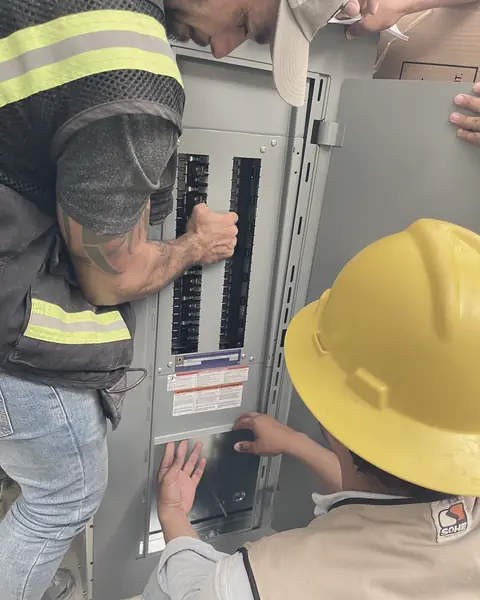 Dos técnicos con casco conectan interruptores en un tablero de distribución