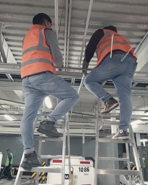 Dos técnicos con chaleco sobre escaleras tienden cable por las charolas del techo